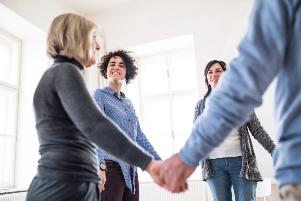 Group of people standing in a circle and holding hands during therapy.